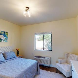 A minimalist bedroom with a bed, chair, and artwork beside a window.