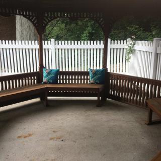 A cozy gazebo with wooden benches and blue cushions, surrounded by a white fence.