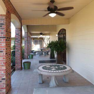 A spacious outdoor patio featuring a decorative table, ceiling fan, and lush greenery, perfect for relaxation.