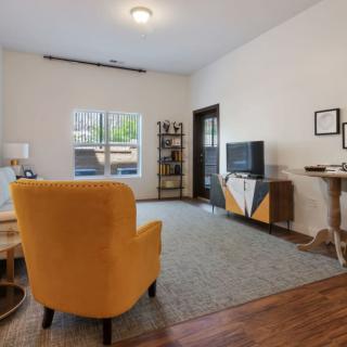 A modern living room featuring a vibrant yellow chair, hardwood flooring, and a sleek entertainment center with a TV.