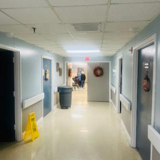 A view of a hallway in a hospital, showing rooms and a cleaning caution sign on the floor.