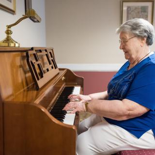 An elderly woman playing the piano indoors.