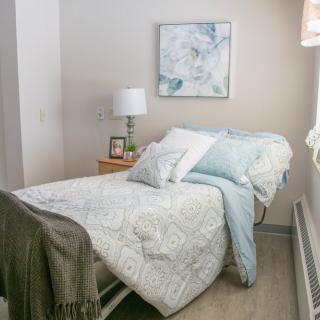 A cozy bedroom with minimalist decor, featuring a neatly made bed, a lamp on the bedside table, and a piece of artwork on the wall.