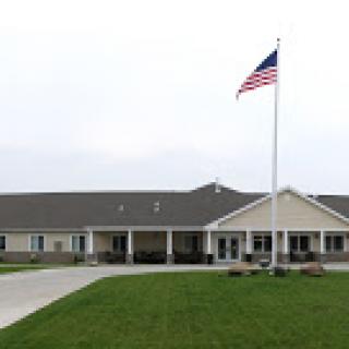 A modern facility with an American flag in front, set against a grassy landscape.