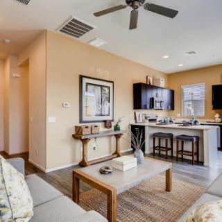 A cozy and modern living room with an open kitchen setup, featuring stylish furniture and a ceiling fan.