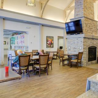 A cozy living and dining area featuring a stone fireplace, a mounted television, and wooden chairs around tables.