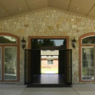 A building entrance with a stone facade, featuring a central doorway and large windows on either side.