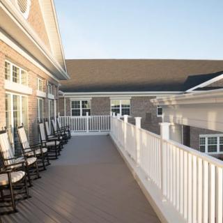 A spacious outdoor deck with white railings and several rocking chairs, attached to a residential building.