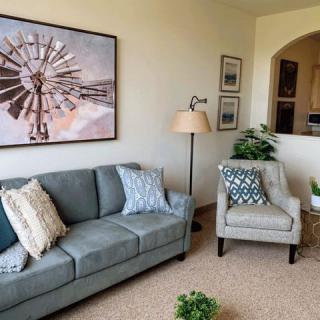 A cozy living room featuring a couch with decorative cushions, an armchair, a floor lamp, and wall art.