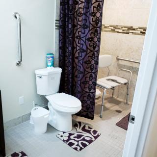 A bathroom with a toilet, shower, and accessibility features including a grab bar and a shower chair.