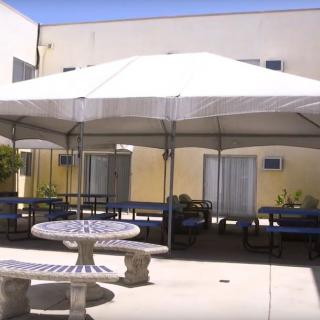 A patio area with tables and benches under a large canopy, adjacent to a building.