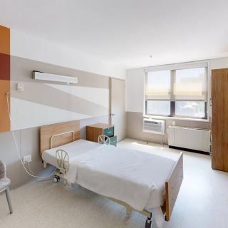 A clean and bright hospital room with a single bed and large window.