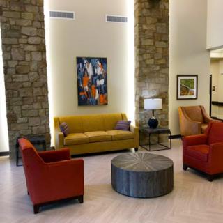 A cozy lobby area featuring a vibrant yellow sofa, red chairs, and a modern coffee table, complemented by stylish artwork on the wall.