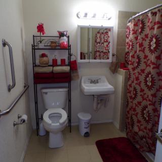 A neatly organized bathroom with a red and white color theme, featuring a toilet, sink, mirror, and shower curtain.