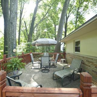A cozy outdoor patio with chairs, a table, and an umbrella, surrounded by lush trees.