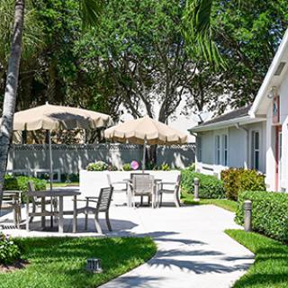 A serene garden patio with tables, chairs, and umbrellas surrounded by lush greenery.
