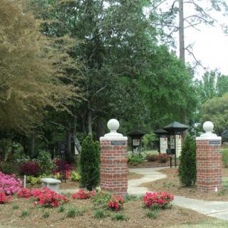 A scenic garden with a brick gateway, vibrant flowers, and a winding pathway through the trees.