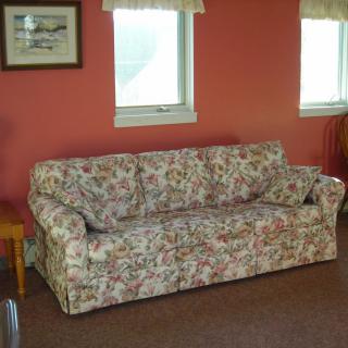 A vintage floral couch placed in a cozy living room with red walls and natural light.