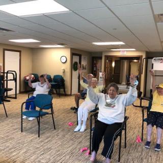 A group of seniors participating in a seated exercise class indoors.