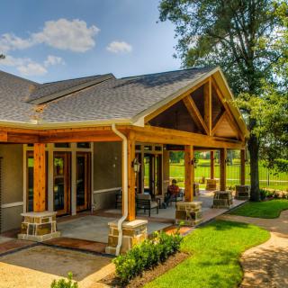 A beautiful house with a wooden porch surrounded by lush greenery and trees.