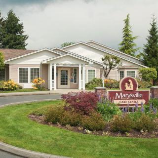 A landscaped entrance to a building with a prominent sign in front, surrounded by trees and gardens.