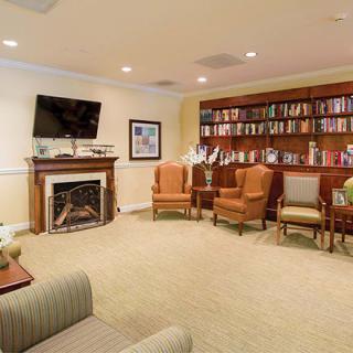 A cozy library with a seating area, featuring armchairs and a television above the fireplace.