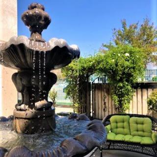 A tranquil garden patio featuring a beautiful stone fountain and cozy green cushioned seating.