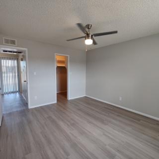 An empty room with wood flooring and a ceiling fan, featuring a doorway leading to another area.