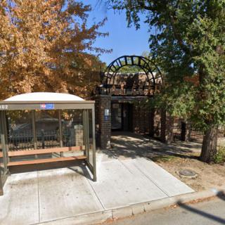 A bus stop with a bench in front of an entrance surrounded by autumn trees.