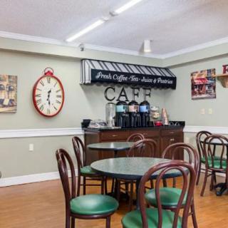 A cozy cafe interior with round tables, wooden chairs, a large wall clock, and a coffee station.