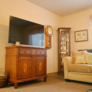 A cozy living room with a wooden cabinet, wall clock, and television beside a comfortable sofa.