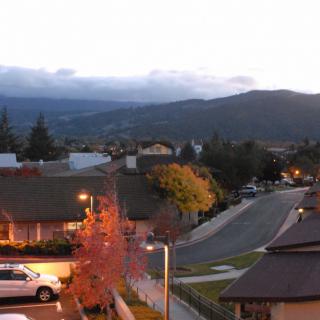 A peaceful suburban neighborhood at dusk with houses lining the street and mountain views in the background.