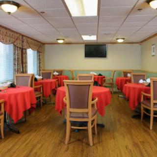 An empty dining room with red tablecloth-covered tables and wooden chairs, featuring a TV on the wall.