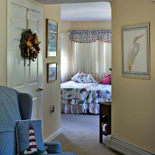 A cozy interior view looking towards a bedroom through a hallway, featuring a decorated wreath on the door and colorful bedspread.