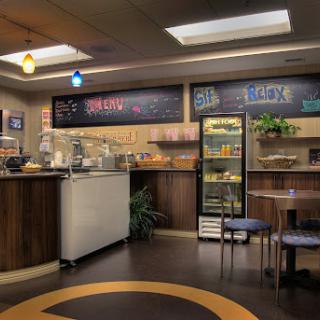 A cozy cafe interior featuring a service counter, display fridge, and comfortable seating.