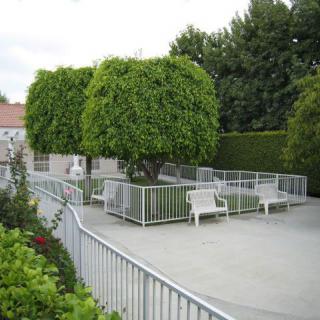 A landscaped garden area with neatly trimmed trees and benches enclosed within a fenced section.