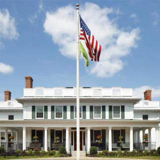 A white building with an American flag on a pole in front, set against a partly cloudy sky.