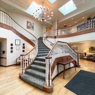A spacious lobby featuring a grand staircase, elegantly designed with wooden railings and a stunning chandelier above.