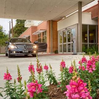 A car parked under a covered entrance with pink flowers in the foreground.