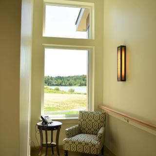 A cozy reading nook by a large window with natural light streaming in, featuring a patterned chair, side table, and wall lamp.