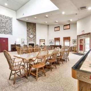 A spacious lounge area with wooden furniture, featuring a large dining table and chairs, a stone fireplace, and recreational amenities.