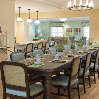 A well-decorated dining room with a long table and multiple chairs, set for a meal, featuring elegant lighting and decor.