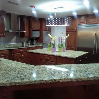 A modern kitchen with granite countertops and wood cabinets, featuring stainless steel appliances and pendant lighting.