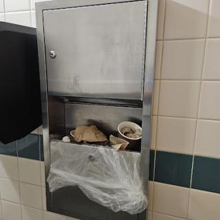 A metal trash receptacle overflowing with waste in a restroom.
