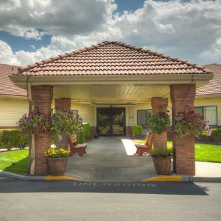 A welcoming entrance to a building with potted plants and a tiled roof under a partly cloudy sky.
