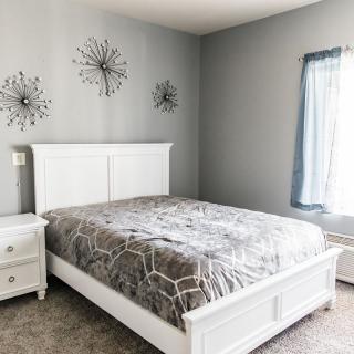 A minimalist bedroom with white furniture and gray walls.