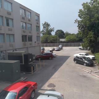 A view of a parking lot adjacent to a building, featuring various vehicles and greenery.
