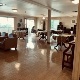 A spacious dining room with tables and chairs arranged neatly, featuring large windows that let in natural light.