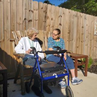 Two women sitting outdoors, engaging in conversation with a walker nearby.