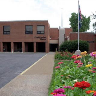 A view of a school building surrounded by colorful flowers and a flagpole.